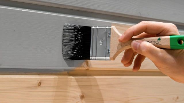 Hand die met een kwast een houten schuurwand beitst