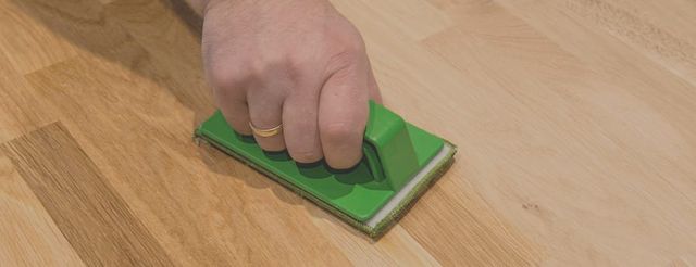 Hand die met een groene pad een houten vloer plaatselijk bijwerkt