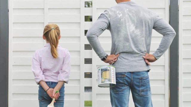 Twee mensen bekijken een wit geverfde schutting met een verfblik