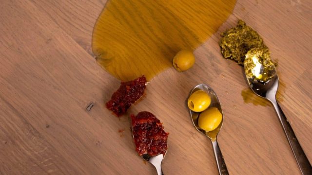Houten tafelblad met vetvlekken en lepels met olie en jam