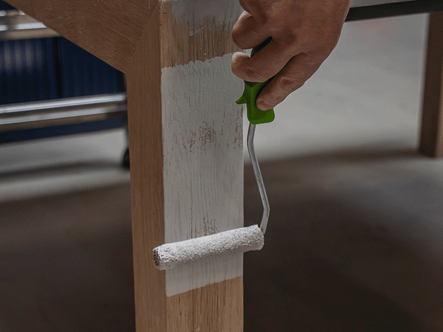 Hand die met een roller een eikenhouten tafelpoot behandelt