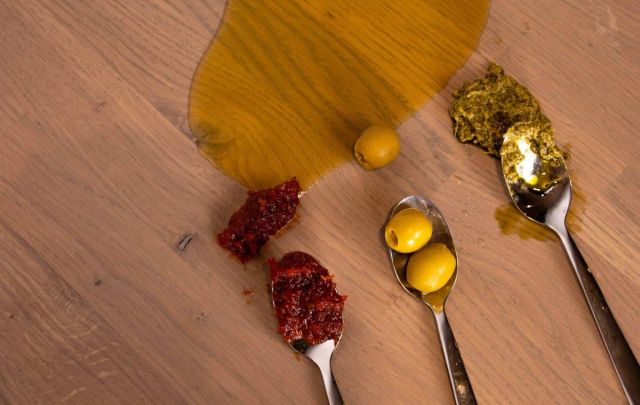 Houten tafelblad met vetvlekken en lepels met olie en jam