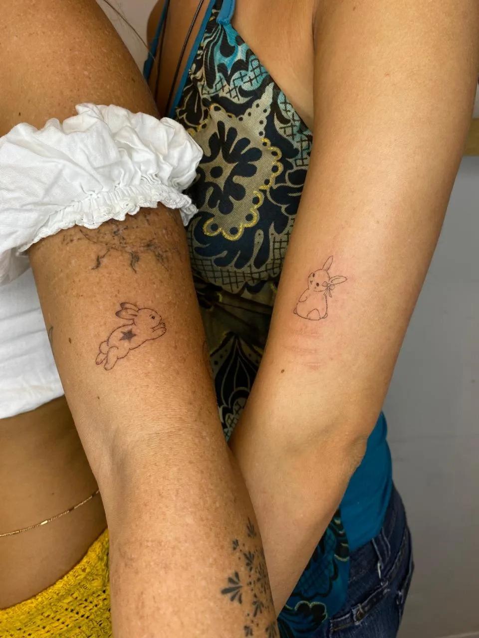 Two people showing matching fine line bunny tattoos on their arms, representing professional custom tattoo work in Budva.