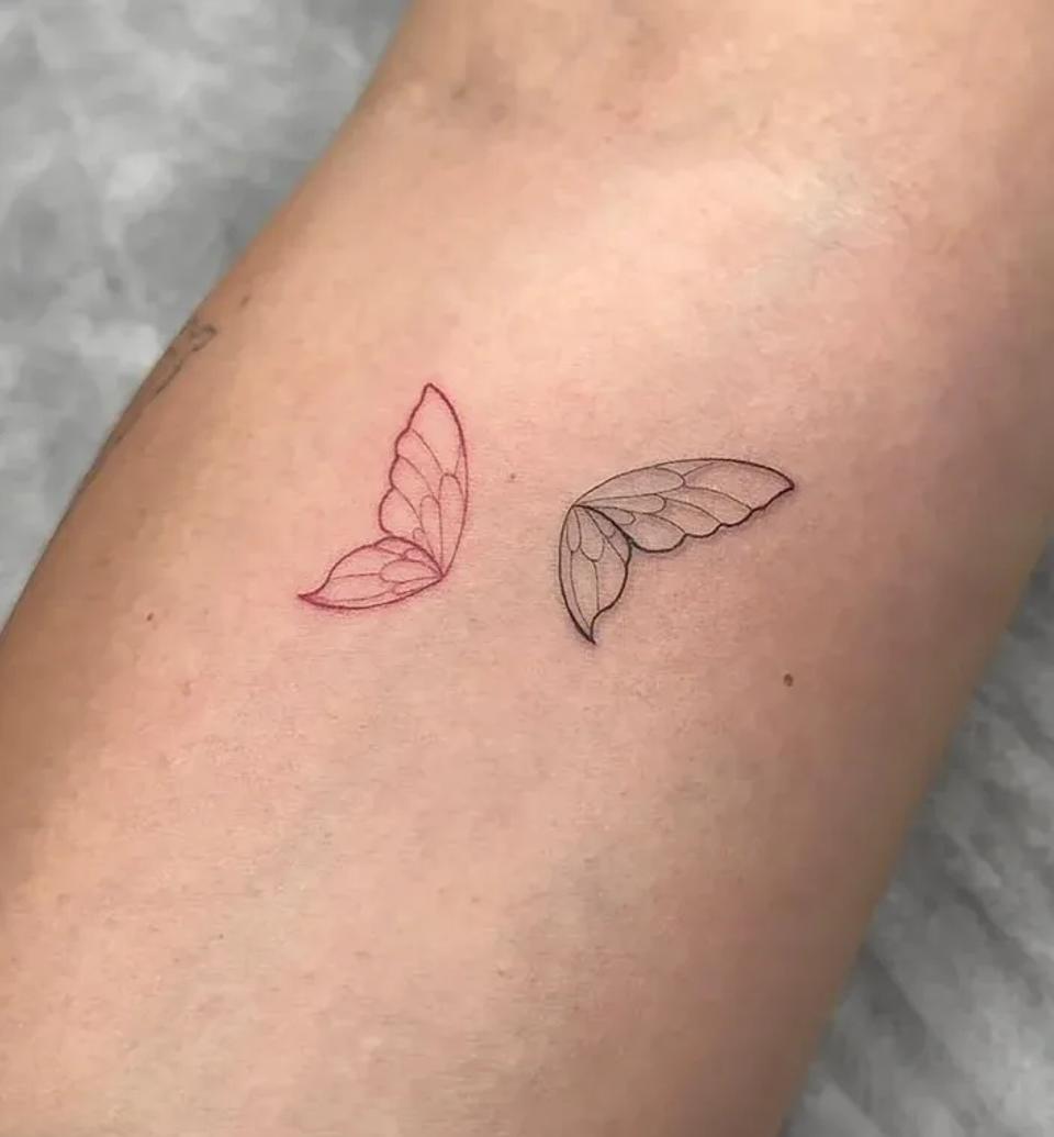 A minimalist fine line tattoo of two delicate butterfly wings, one inked in red and the other in black, crafted at a professional tattoo studio in Budva, Montenegro.