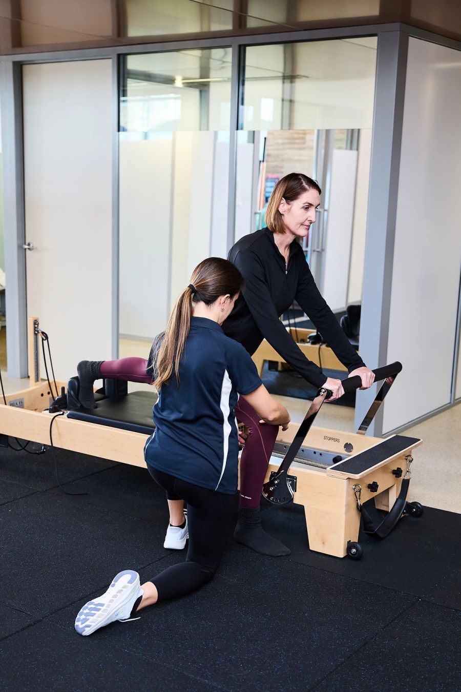 Client kneeling on a Pilates reformer as a physiotherapist guides the exercise