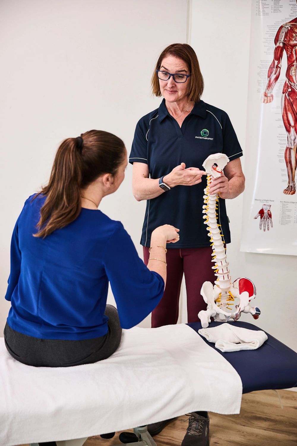 Physiotherapist using a spine model to explain a back problem to a seated patient