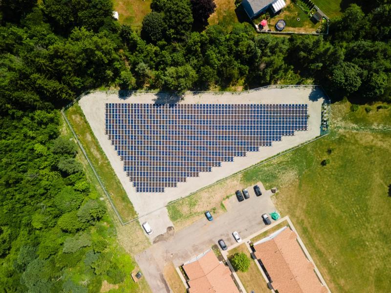 Aerial drone view of the Derby Apartment Complex featuring a ground-mounted solar array supplying clean energy to multi-family buildings, surrounded by green landscape in New York.