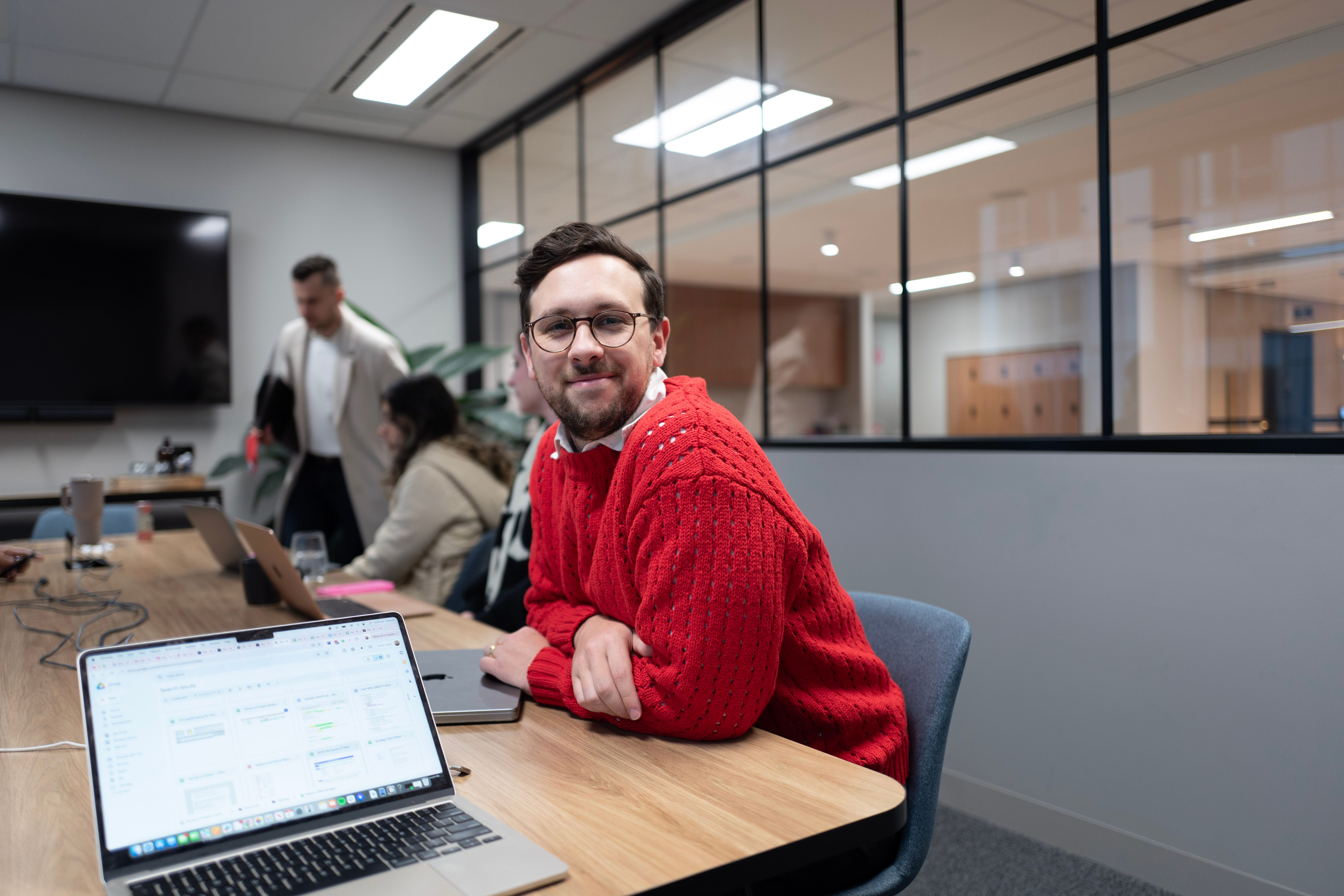 Jacob King Stanley, Director of House of Psalm, in a red knit jumper during a team strategy session in the Melbourne office.