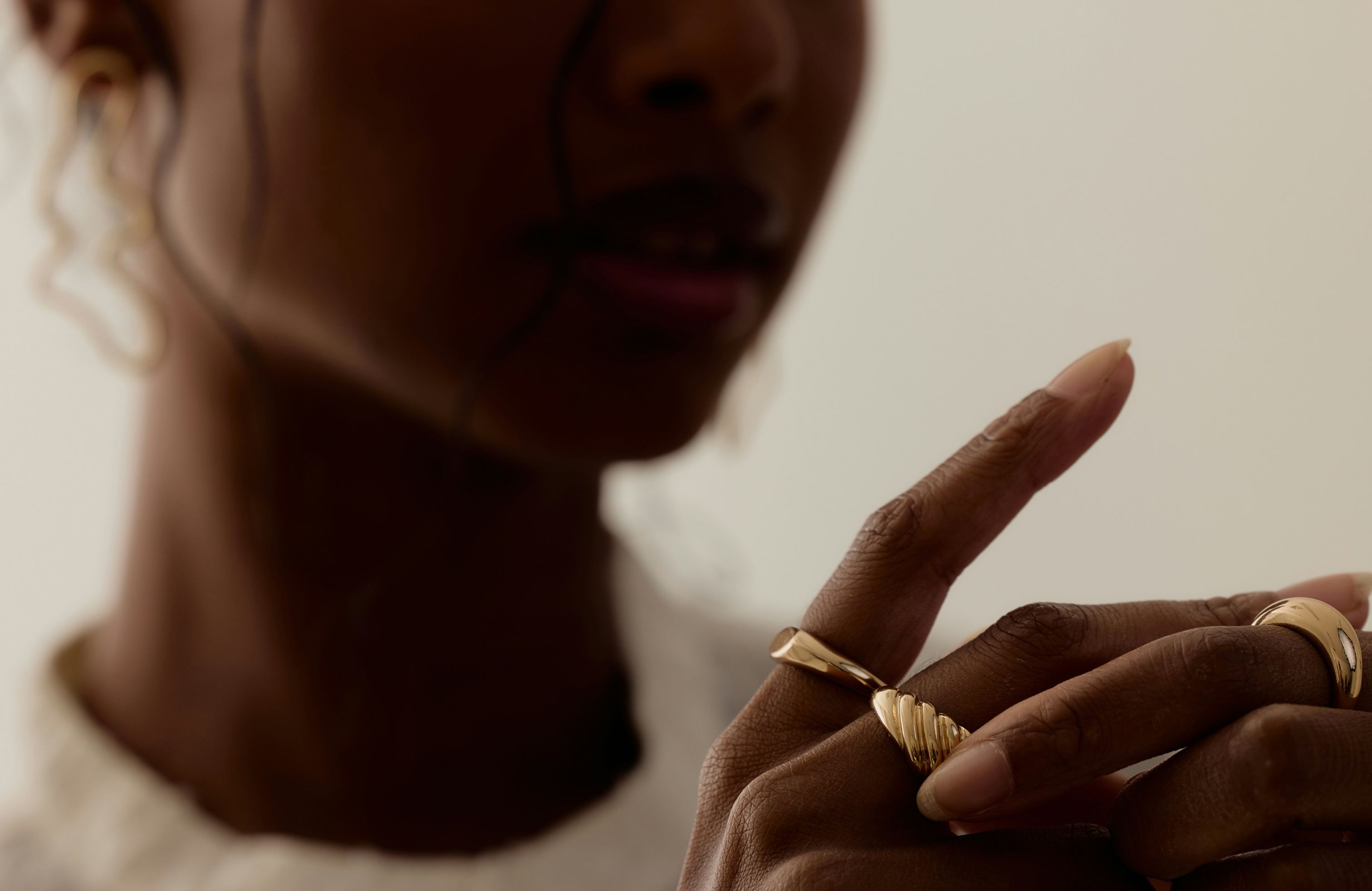 Close-up of a woman’s hand wearing sculptural gold rings, styled with soft natural lighting.