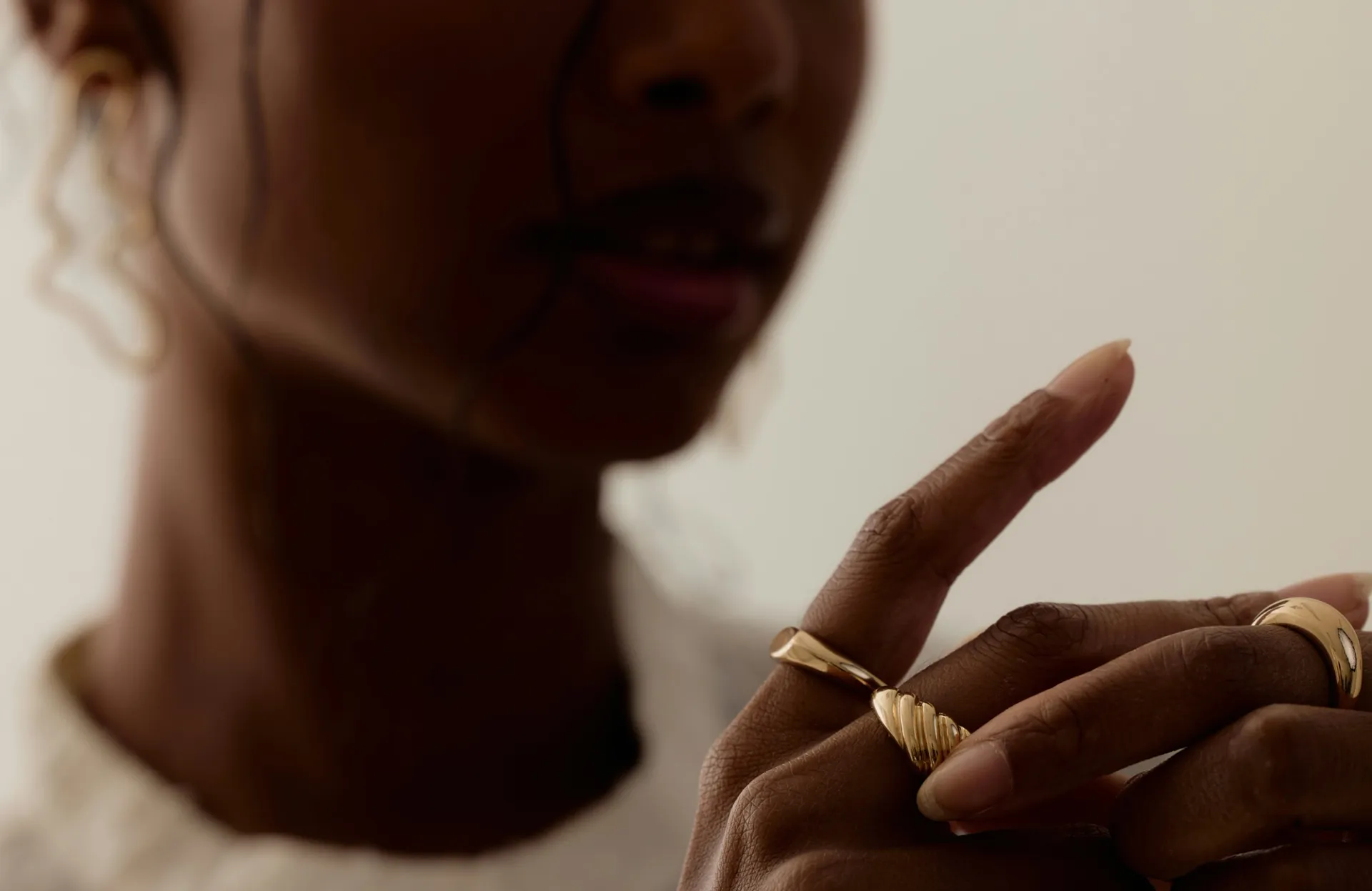 Close-up of a woman’s hand wearing sculptural gold rings, styled with soft natural lighting.