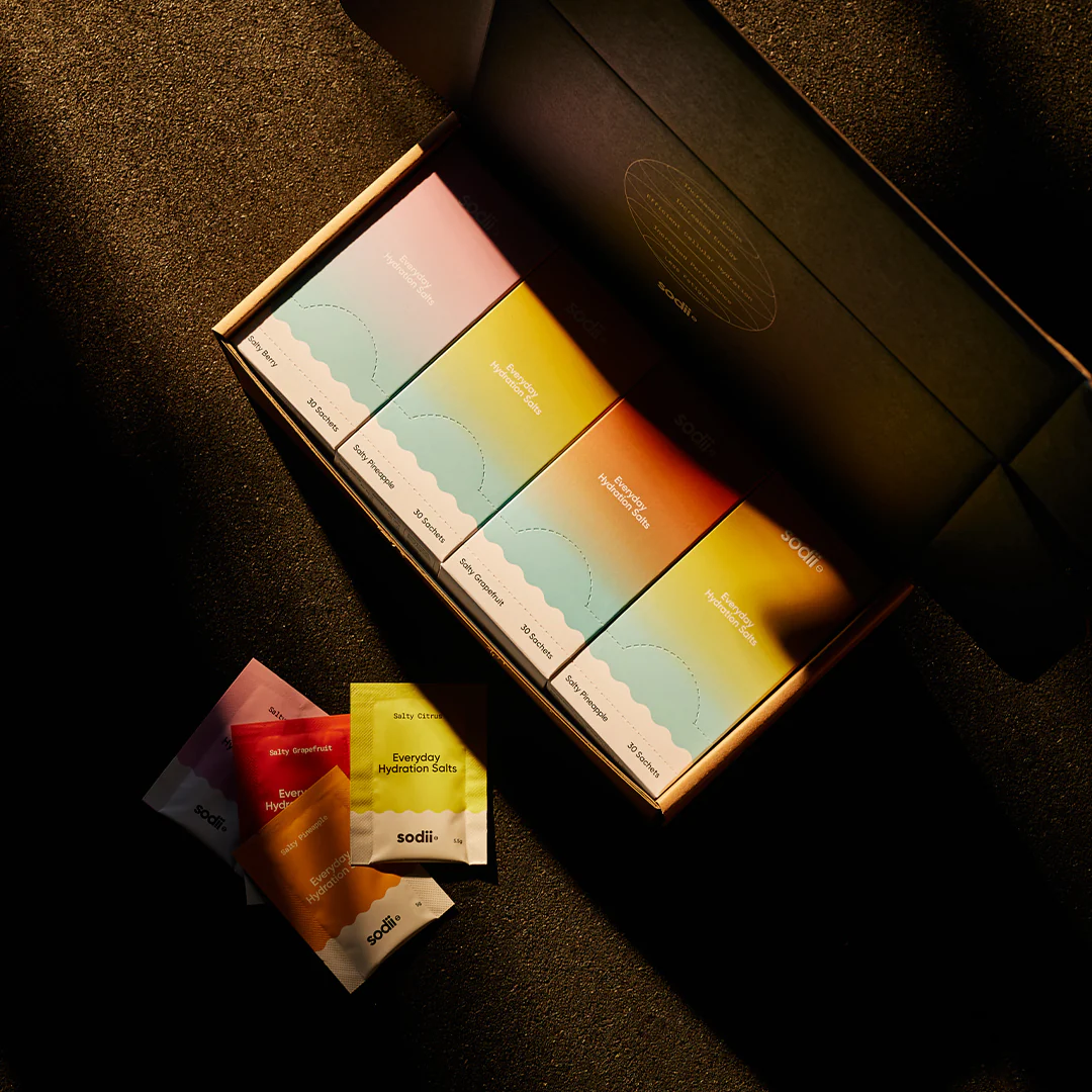 Sodii hydration sachets in a sleek black gift box with individual brightly coloured packs displayed in warm sunlight.