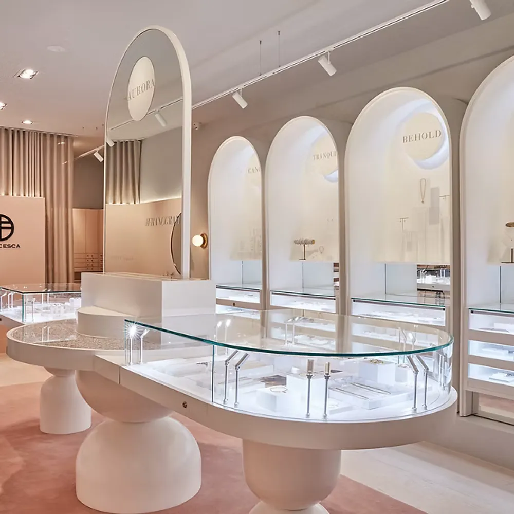 Francesca jewellery boutique interior with modern curved glass displays, soft blush accents and illuminated wall niches showcasing collections like Nomad and Behold