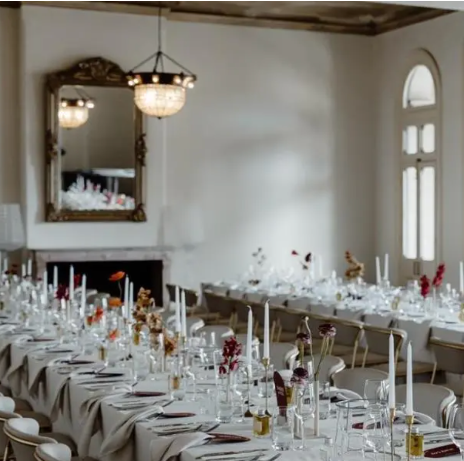 Elegant Venue Now event space with long banquet tables styled with white linens, glassware and minimalist floral arrangements.