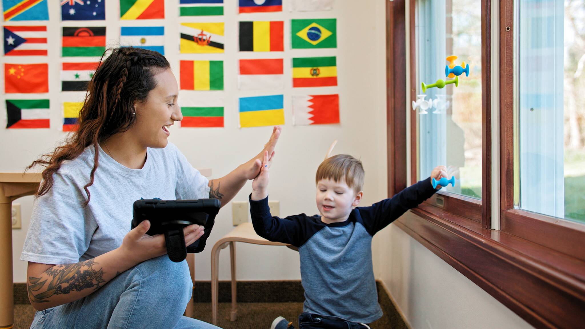 BlueSprig Autism therapist high-fiving a young child during a learning session with flags on the wall