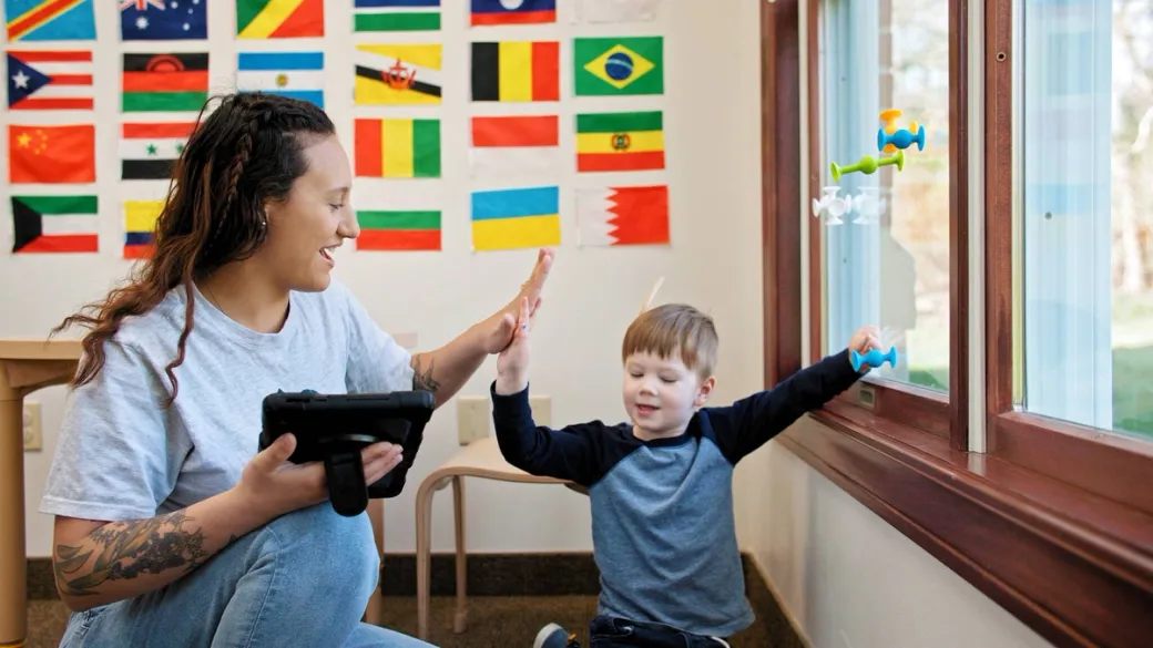 BlueSprig Autism therapist high-fiving a young child during a learning session with flags on the wall
