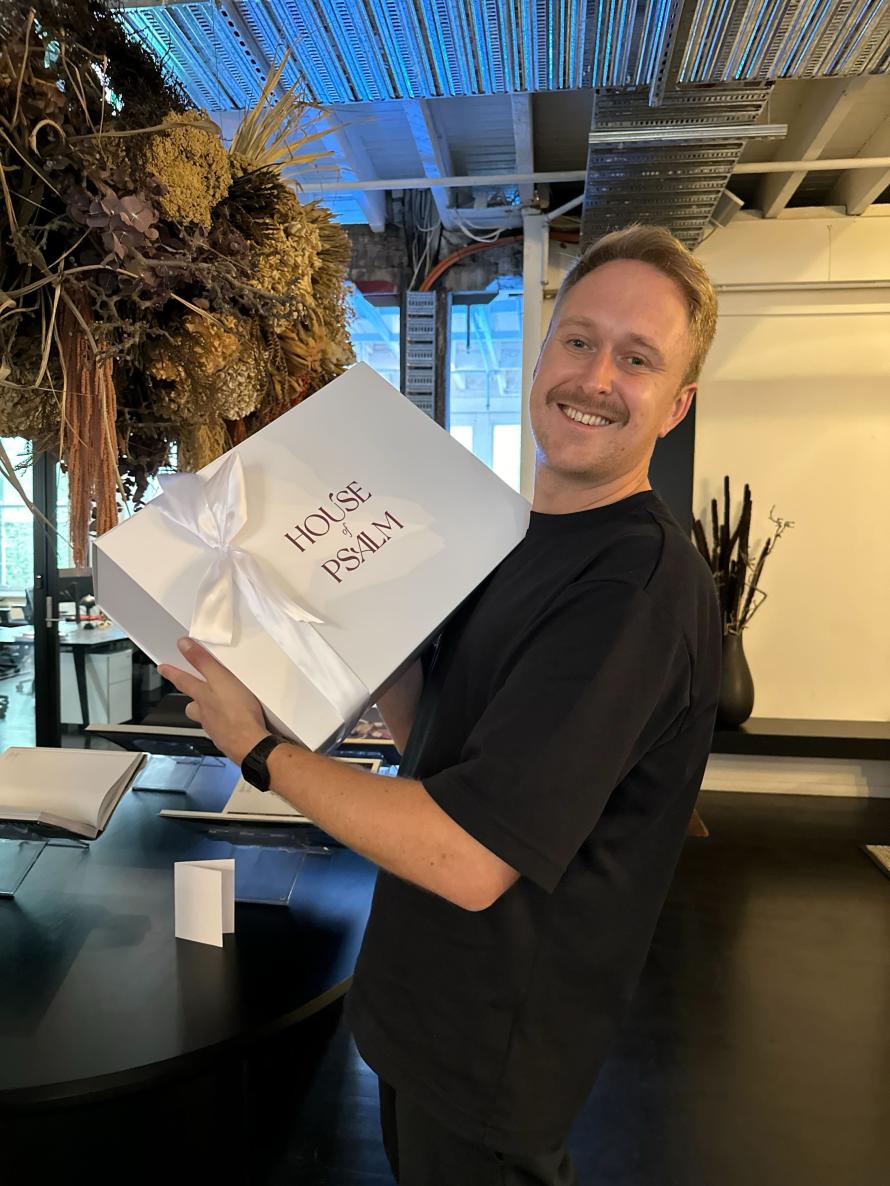Woolly Mammoth partner holding a House of Psalm branded gift box with ribbon inside creative office space
