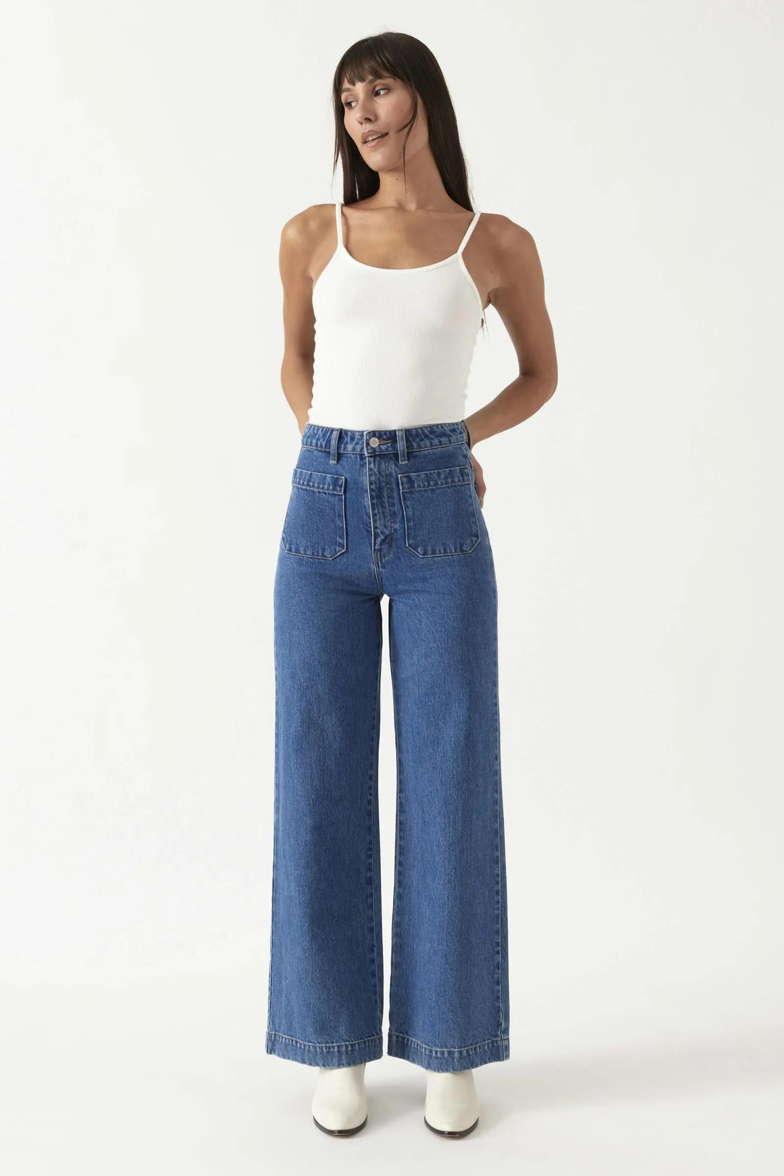 Rolla’s high-waisted wide-leg blue jeans styled with a white tank top and white boots on a plain white background