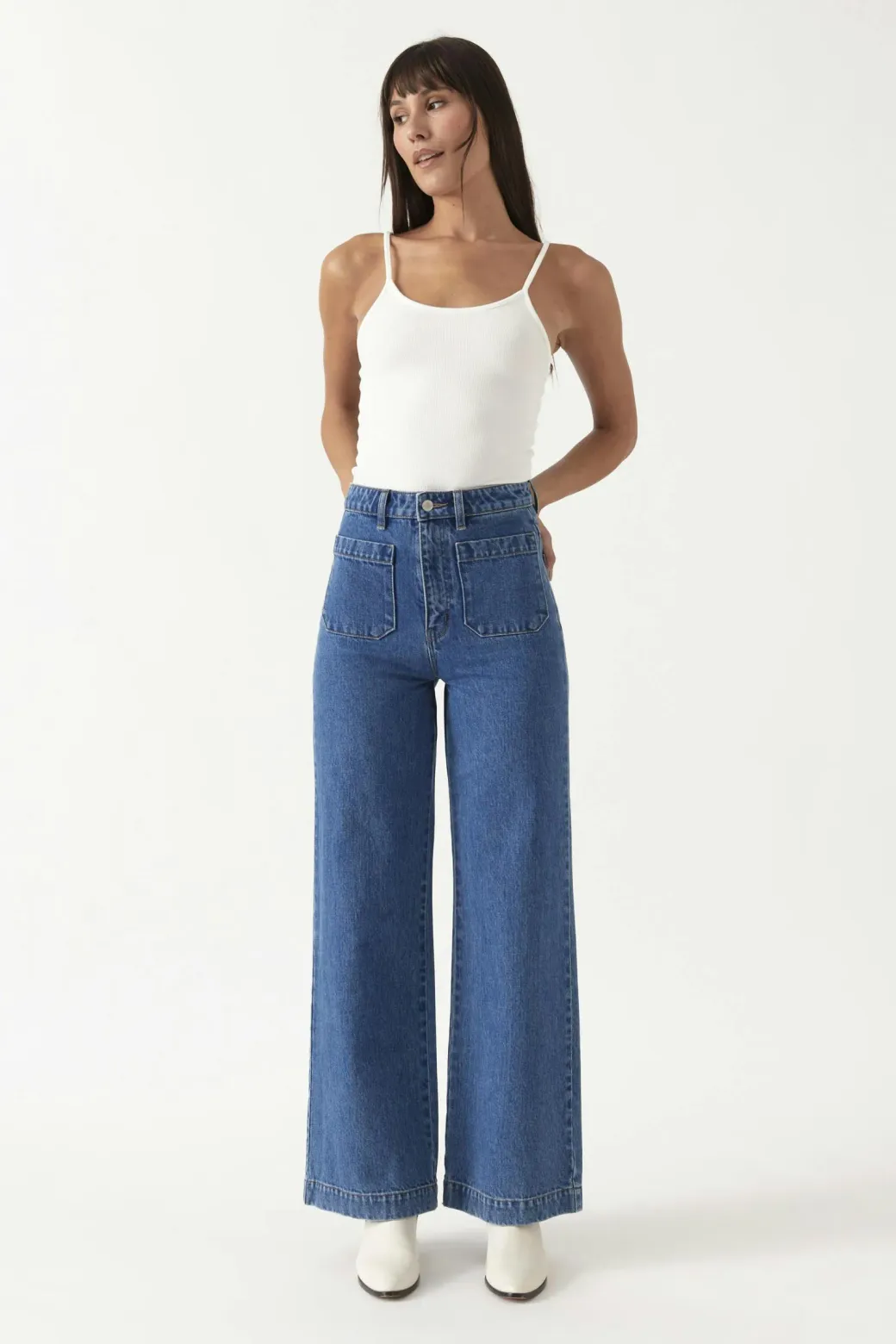 Rolla’s high-waisted wide-leg blue jeans styled with a white tank top and white boots on a plain white background