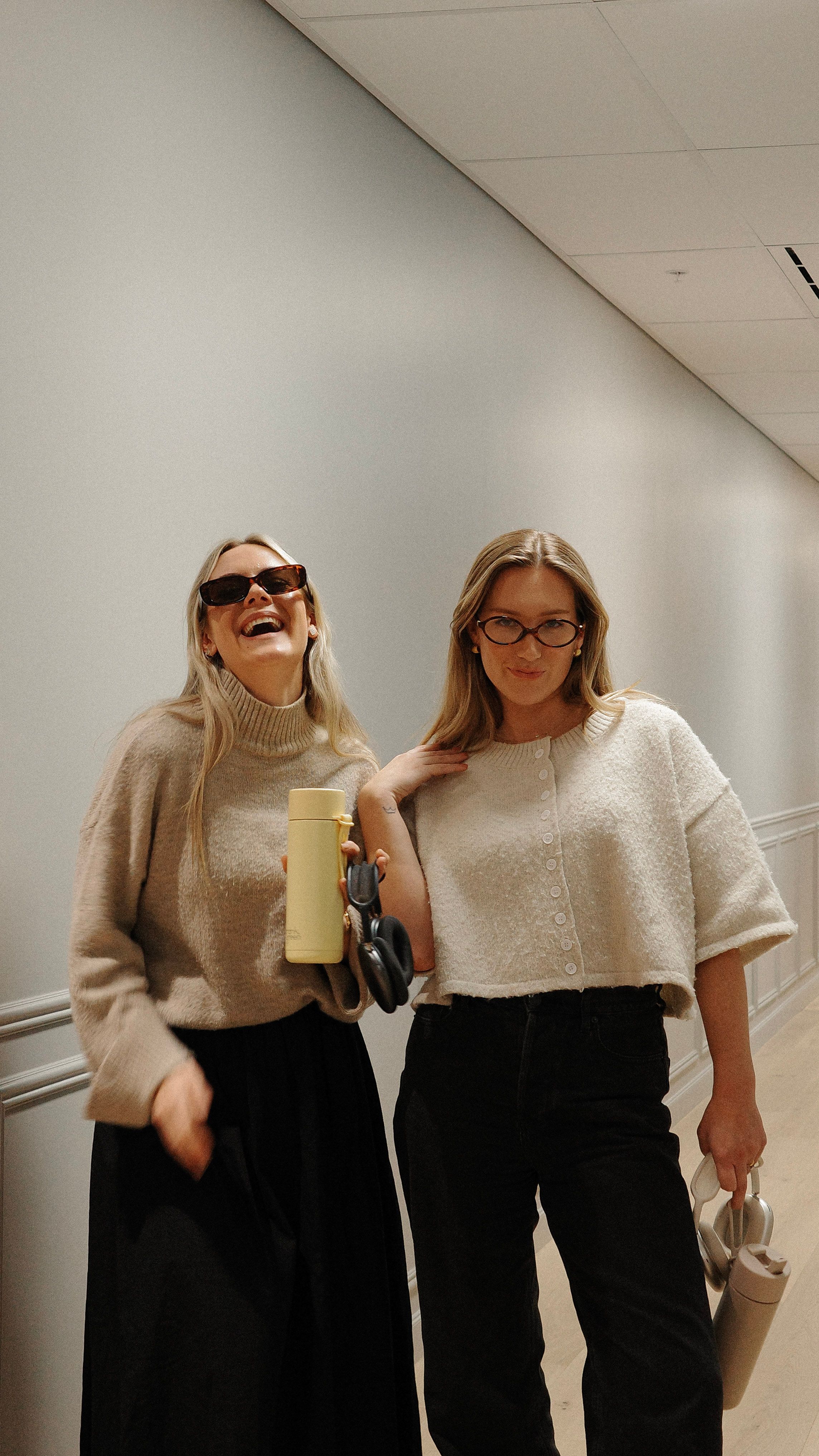 House of Psalm team members laughing in hallway wearing neutral knit sweaters with coffee and water bottles