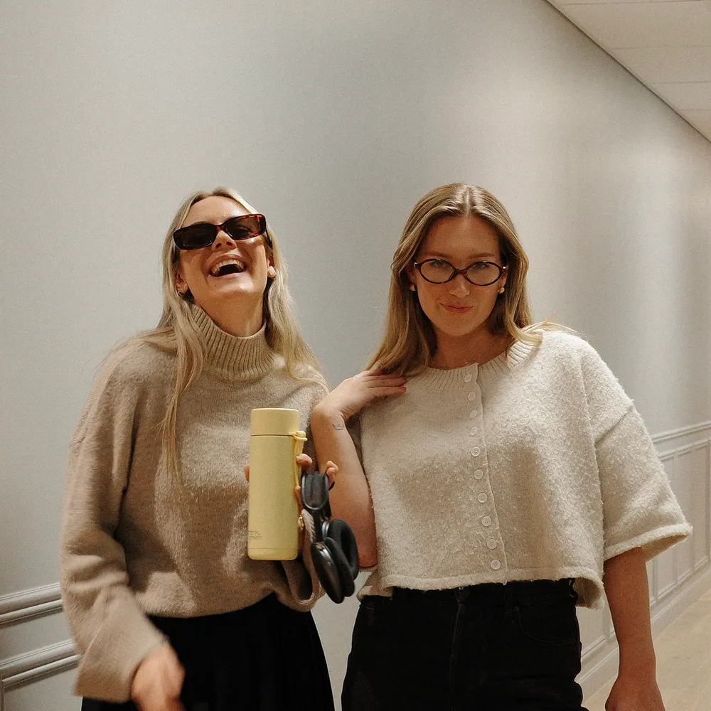 House of Psalm team members laughing in hallway wearing neutral knit sweaters with coffee and water bottles