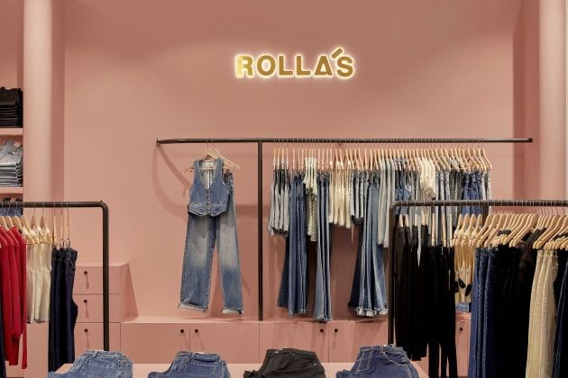 Rolla’s retail store interior featuring denim jeans and tops neatly displayed against a soft pink backdrop with a glowing Rolla’s sign