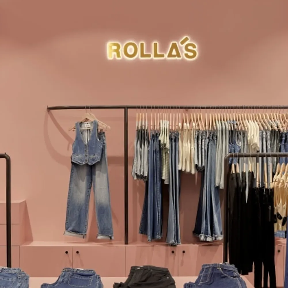 Rolla’s retail store interior featuring denim jeans and tops neatly displayed against a soft pink backdrop with a glowing Rolla’s sign