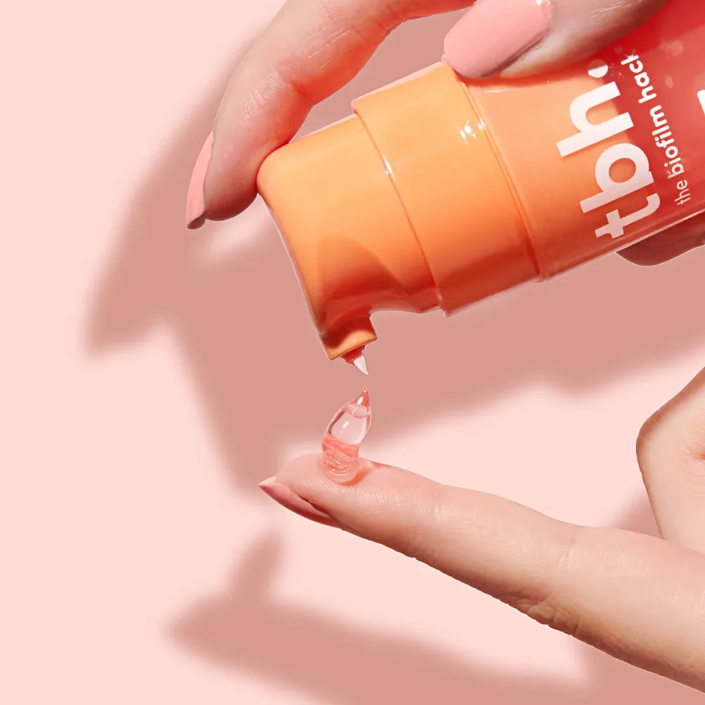 Close-up of tbh Skincare gel cleanser being dispensed onto finger against pastel pink background
