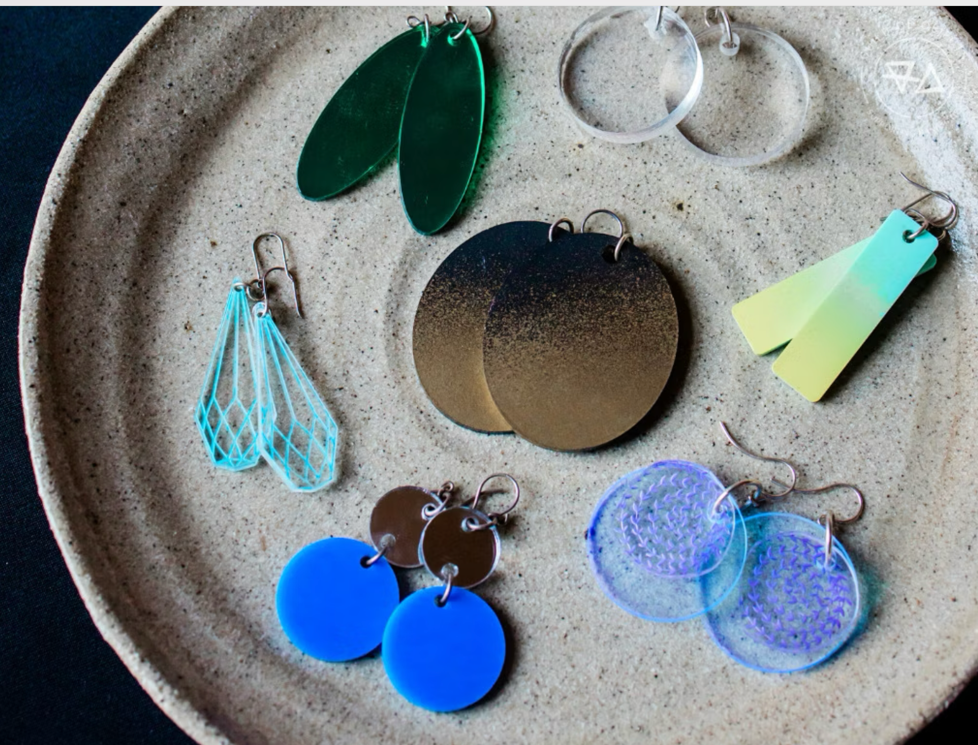 A collection of colorful handmade earrings displayed on a ceramic plate at a We Teach Me jewellery-making class.