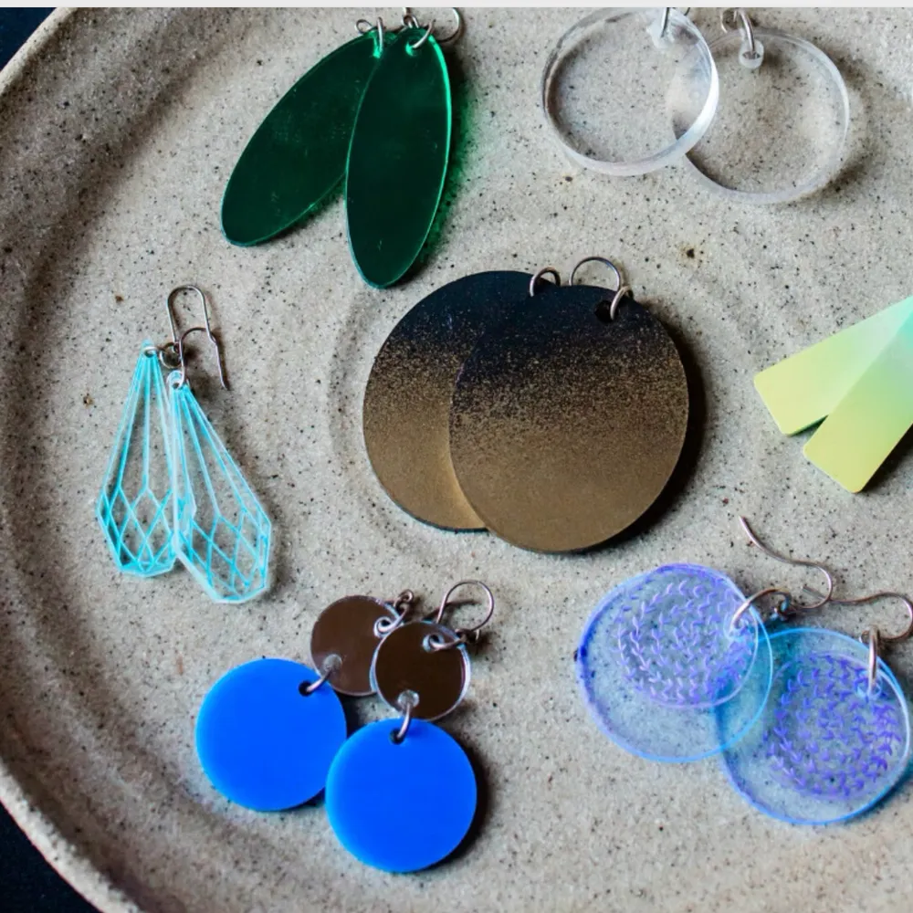 A collection of colorful handmade earrings displayed on a ceramic plate at a We Teach Me jewellery-making class.