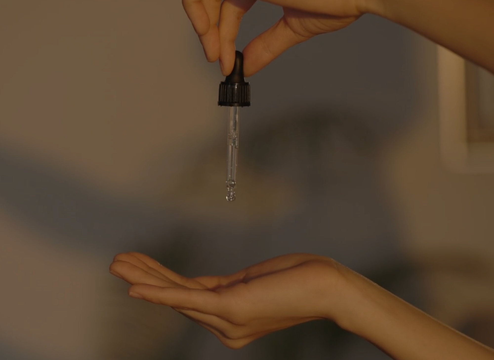 Hand holding skincare dropper releasing serum into palm