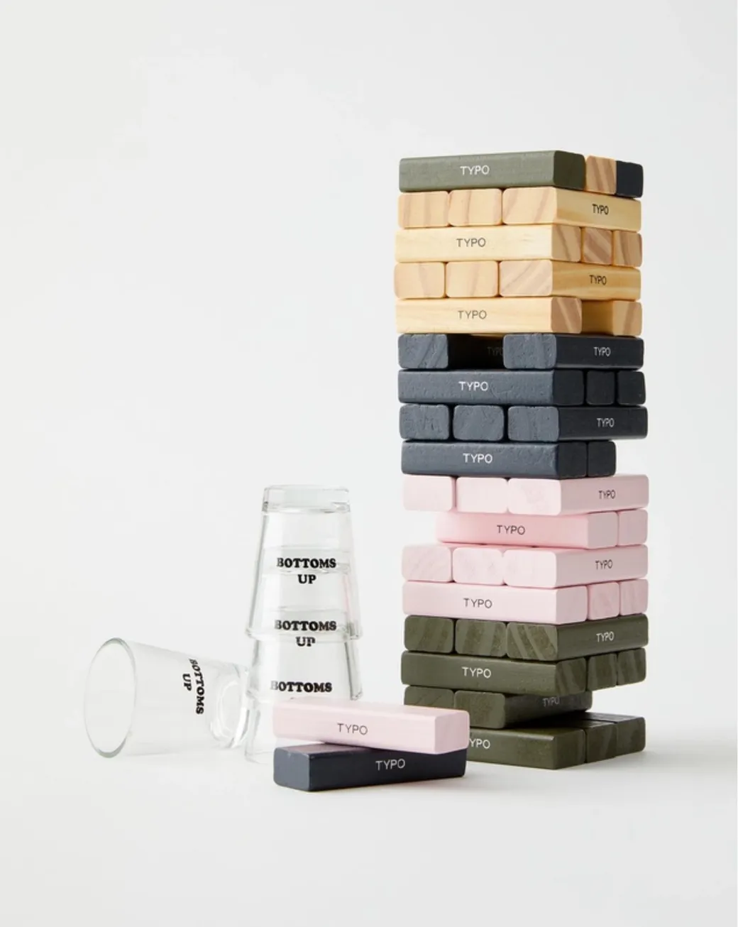 Typo drinking game set featuring colorful Jenga-style blocks in pink, grey, green, and wood tones, with “Bottoms Up” shot glasses on a white background