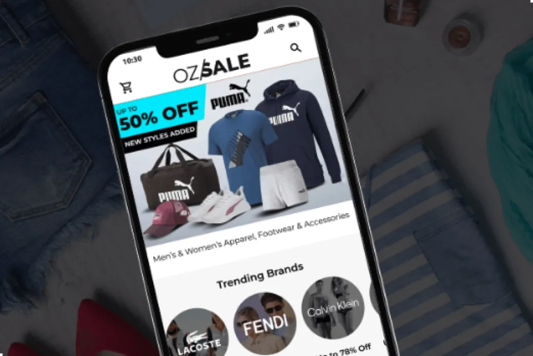 OzSale mobile app open on a smartphone screen, showing Puma apparel and accessories promotion with trending brands like Lacoste, Fendi, and Calvin Klein.