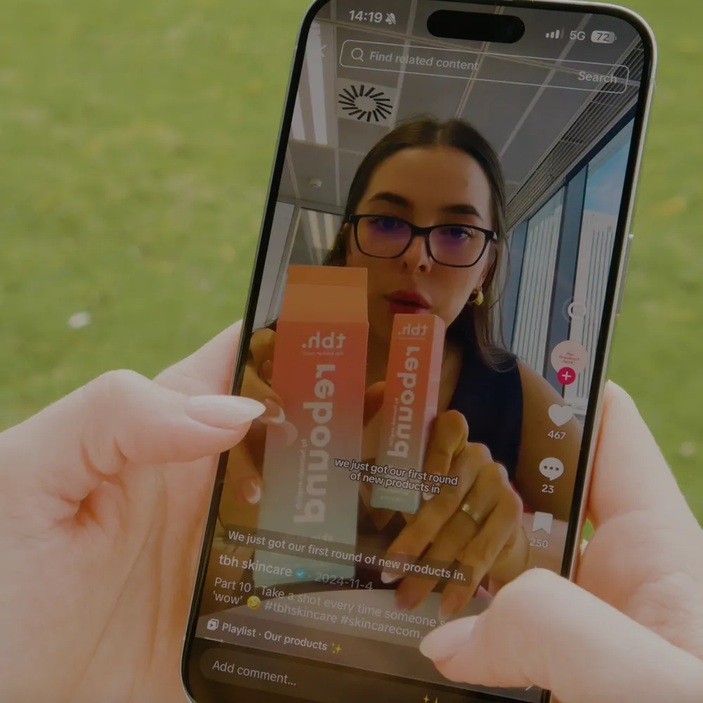 Hand holding a phone showing a TikTok video of a creator reviewing TBH Skincare products, illustrating social media SEO in action.