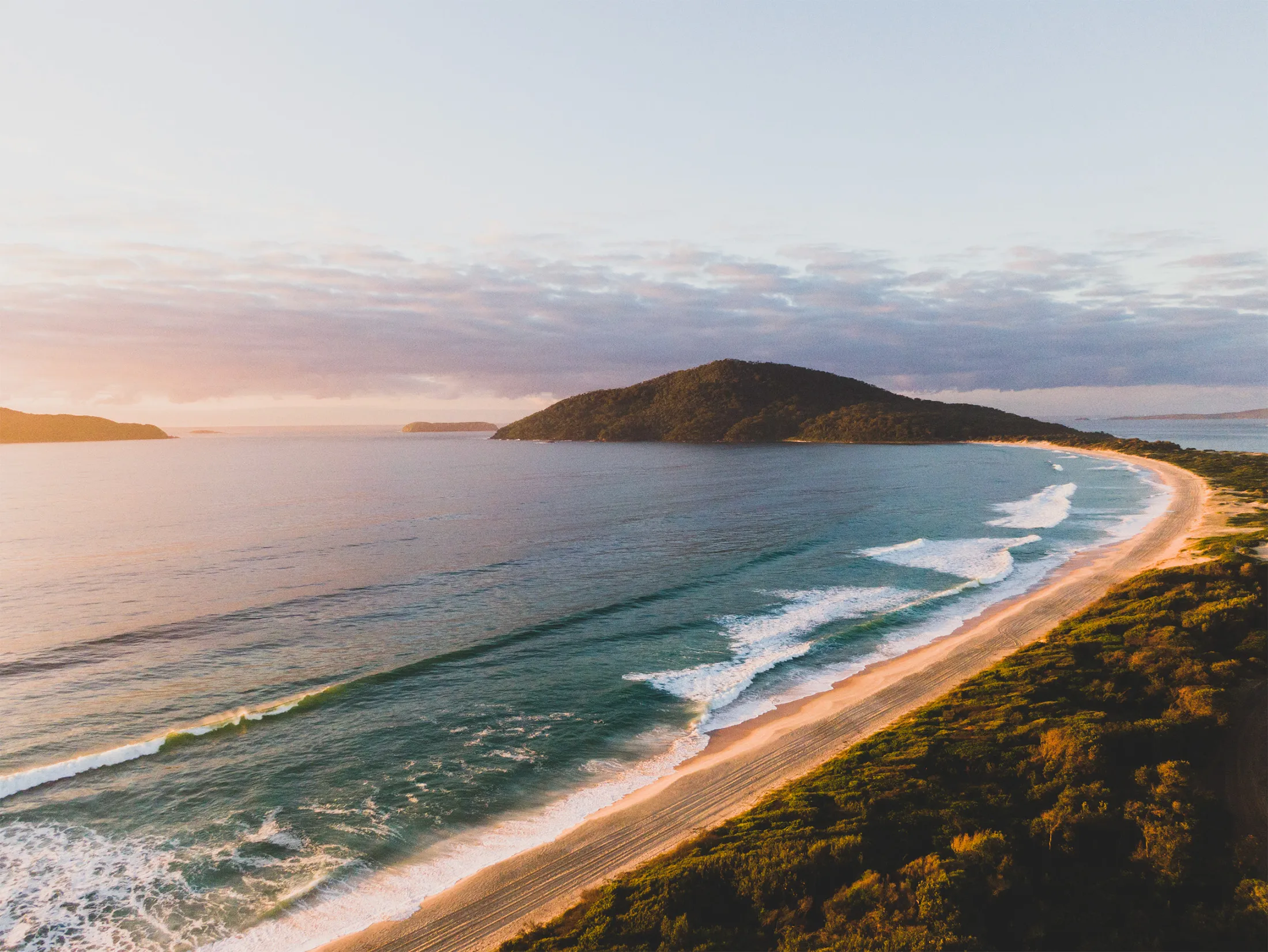 Reflections Holidays coastal landscape with rolling waves and a headland at sunrise.