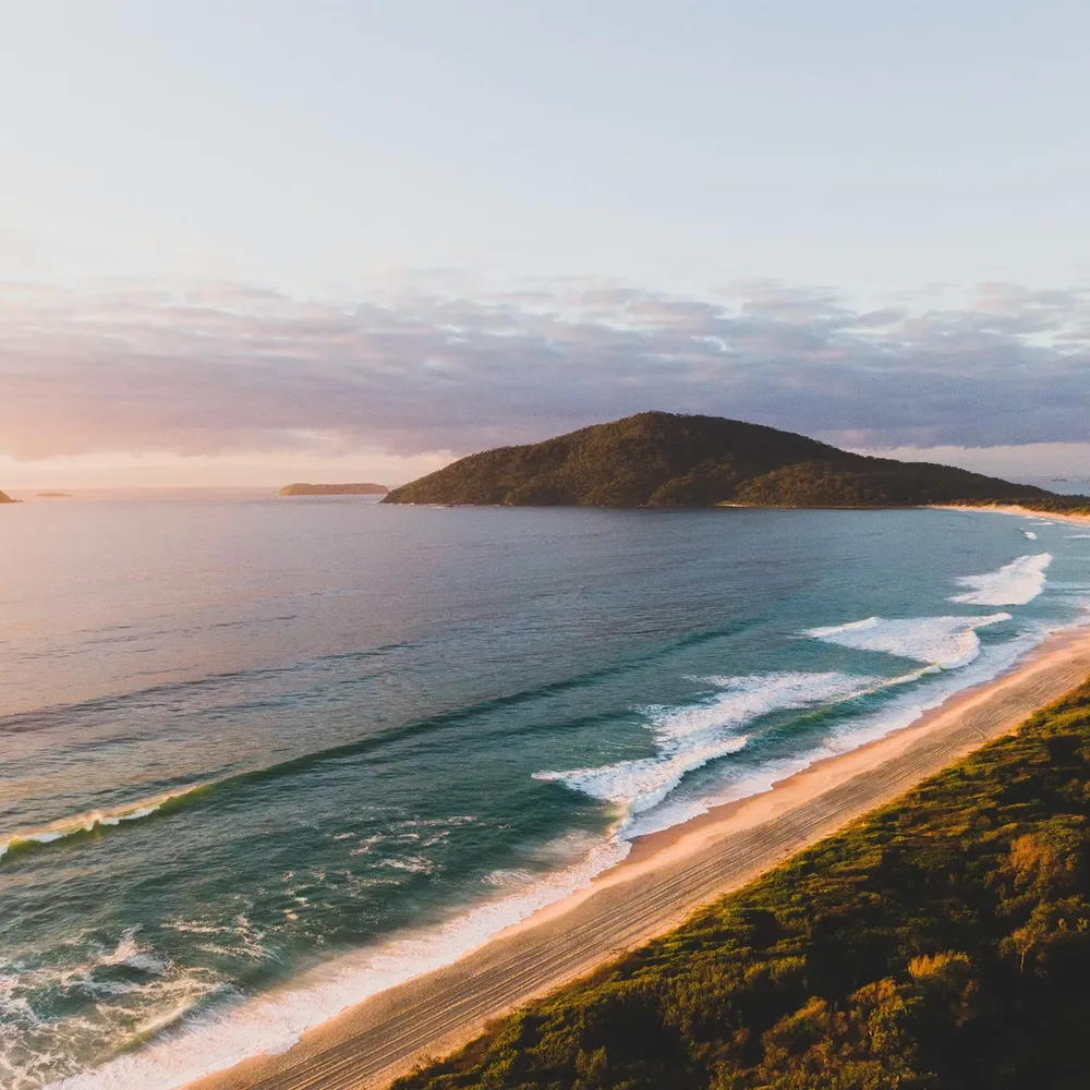 Reflections Holidays coastal landscape with rolling waves and a headland at sunrise.