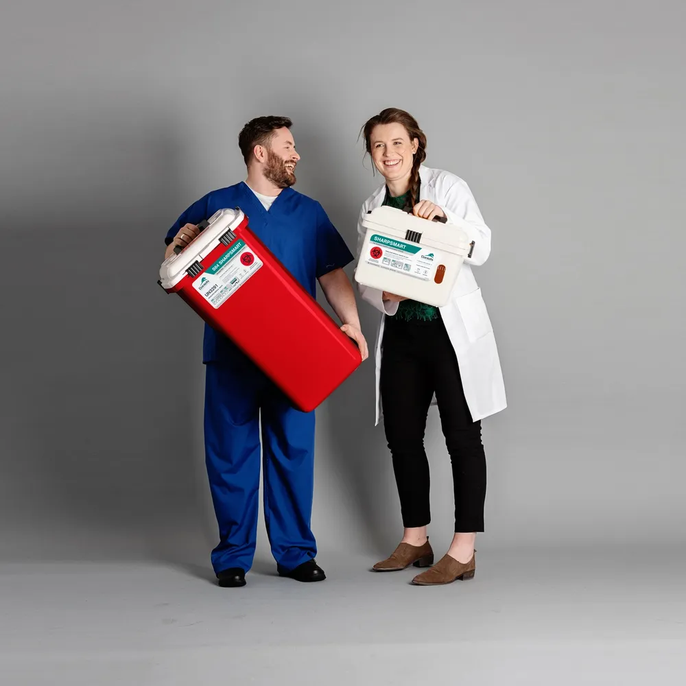 Healthcare staff holding Daniels Health red and white clinical waste containers, standing together in a grey studio setting