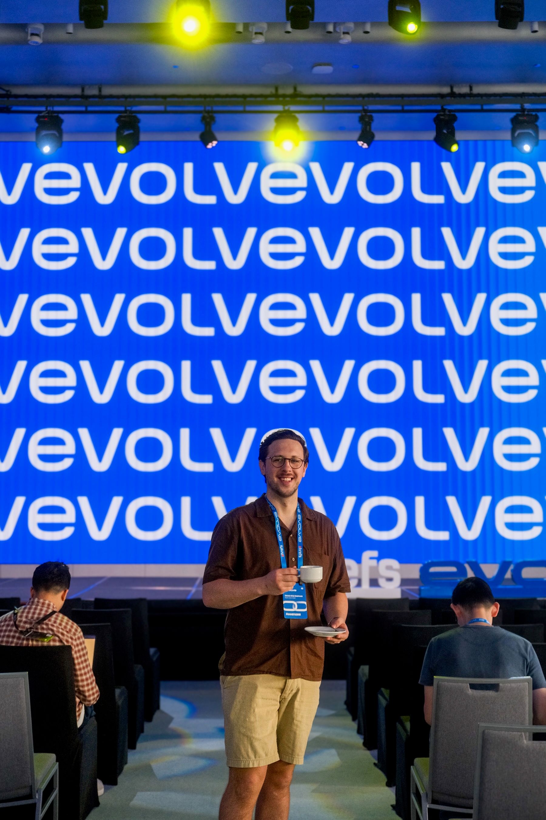 House of Psalm Director standing in front of Evolve conference stage with lanyard and badge in event hall