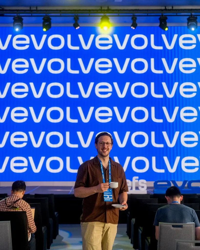 House of Psalm Director standing in front of Evolve conference stage with lanyard and badge in event hall