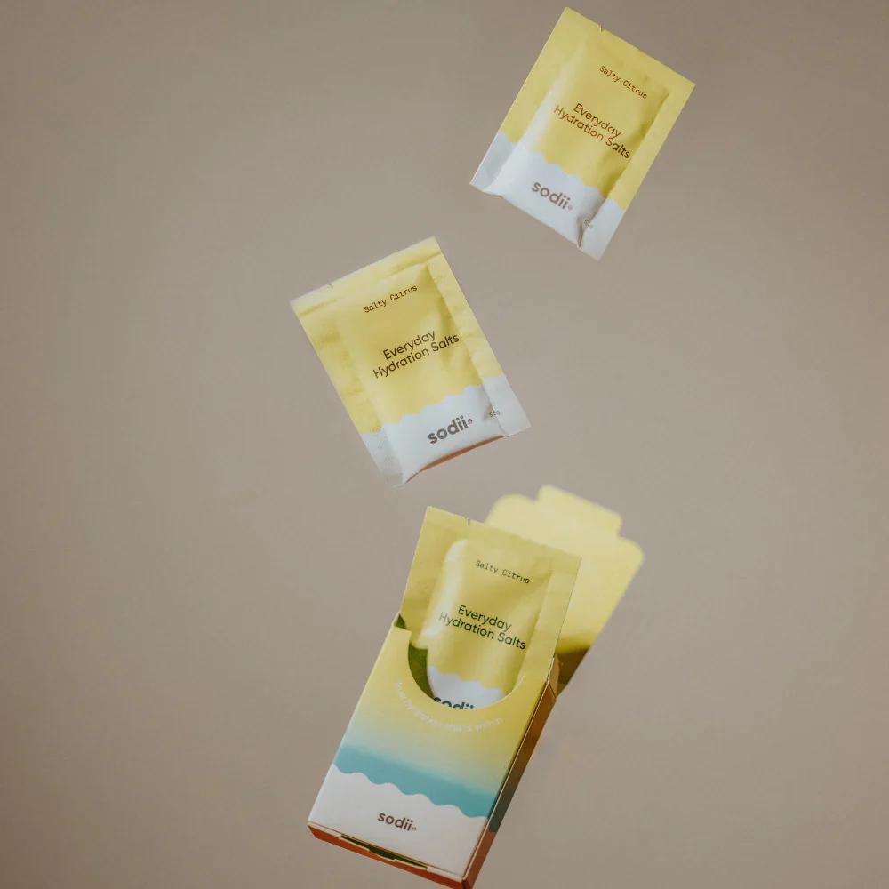 Sodii Everyday Hydration Sachets in yellow packaging, displayed mid-air above the product box.