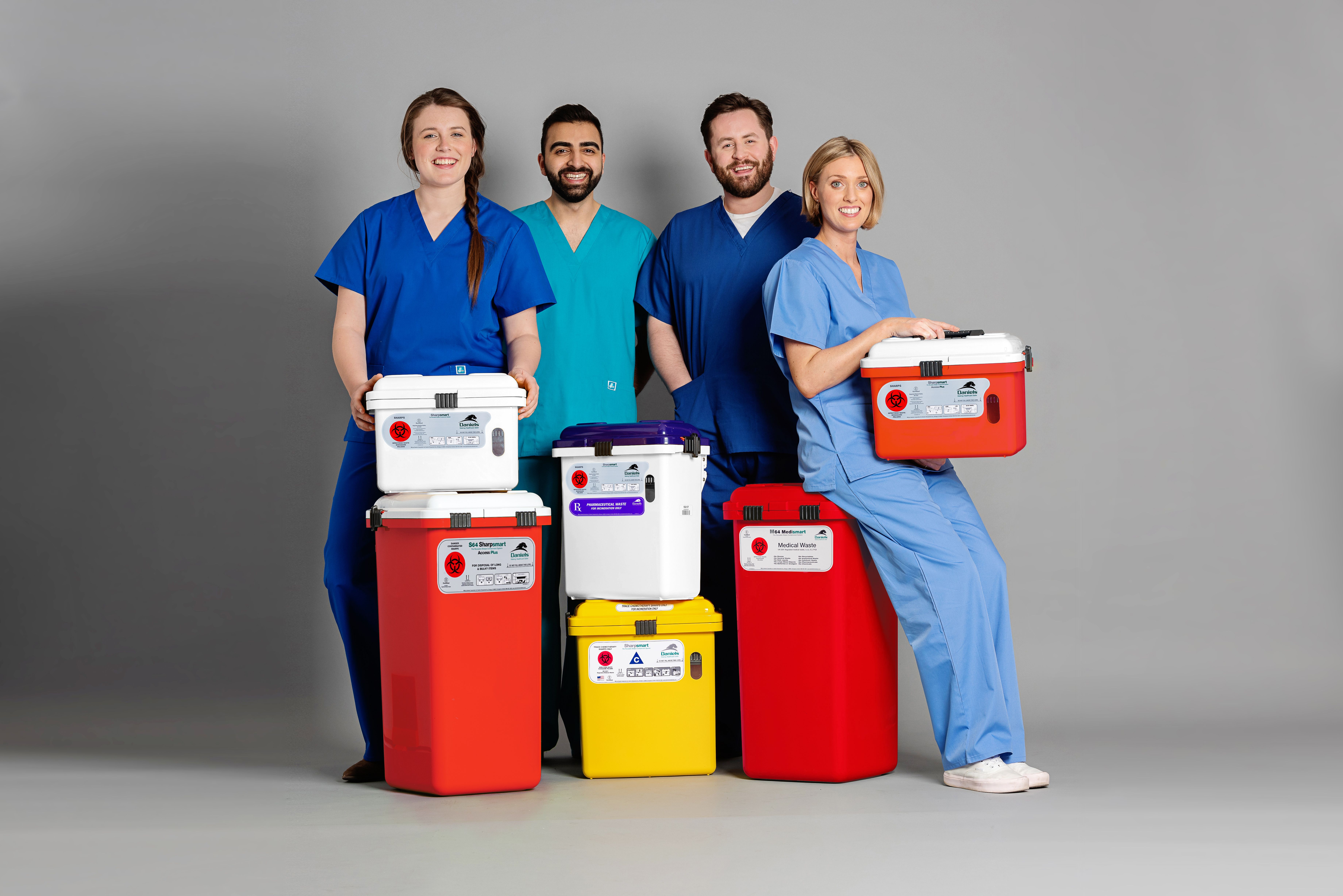 Group of staff in scrubs smiling and posing with  Daniels Health's clinical waste bins in studio setting