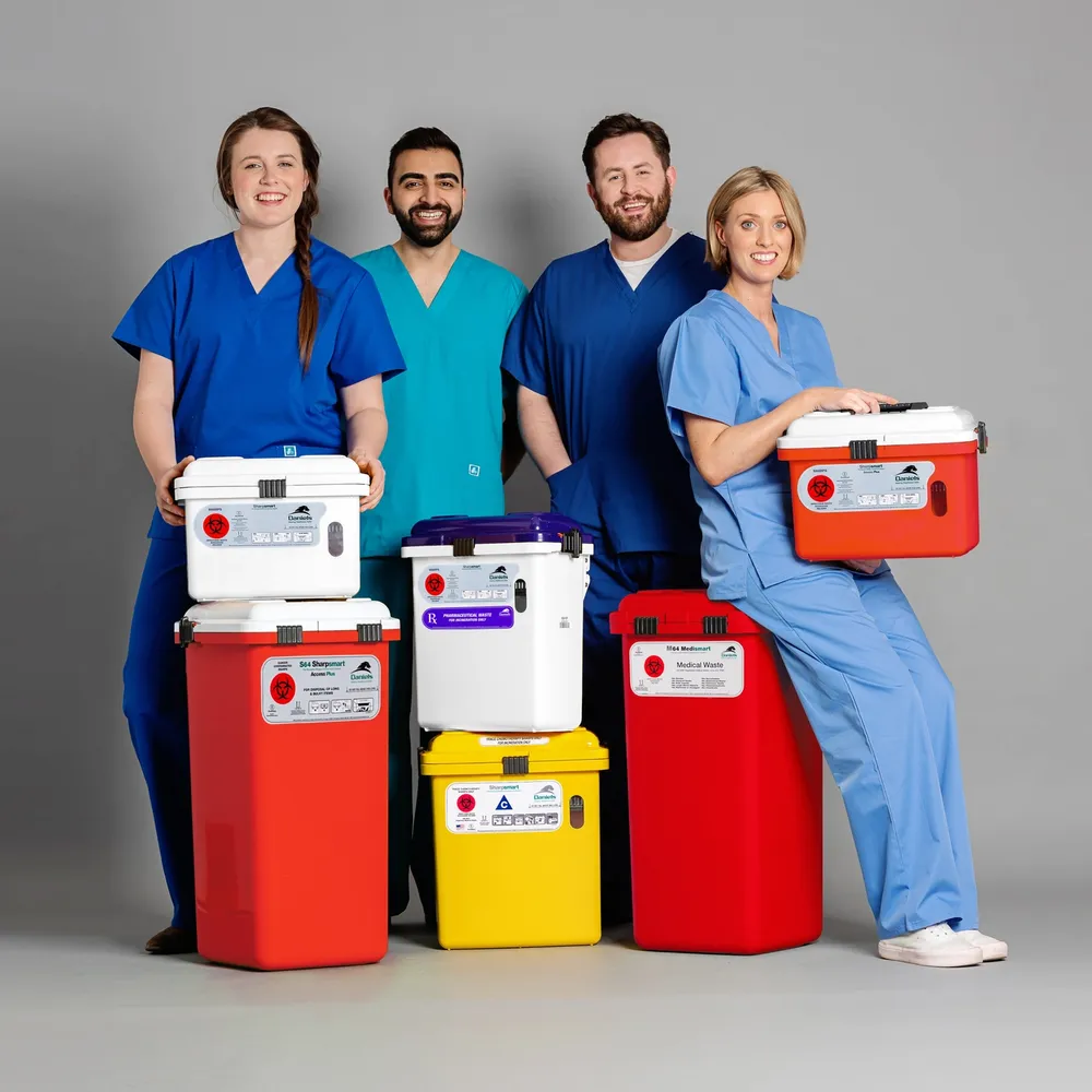Group of staff in scrubs smiling and posing with Daniels Health's clinical waste bins in studio setting