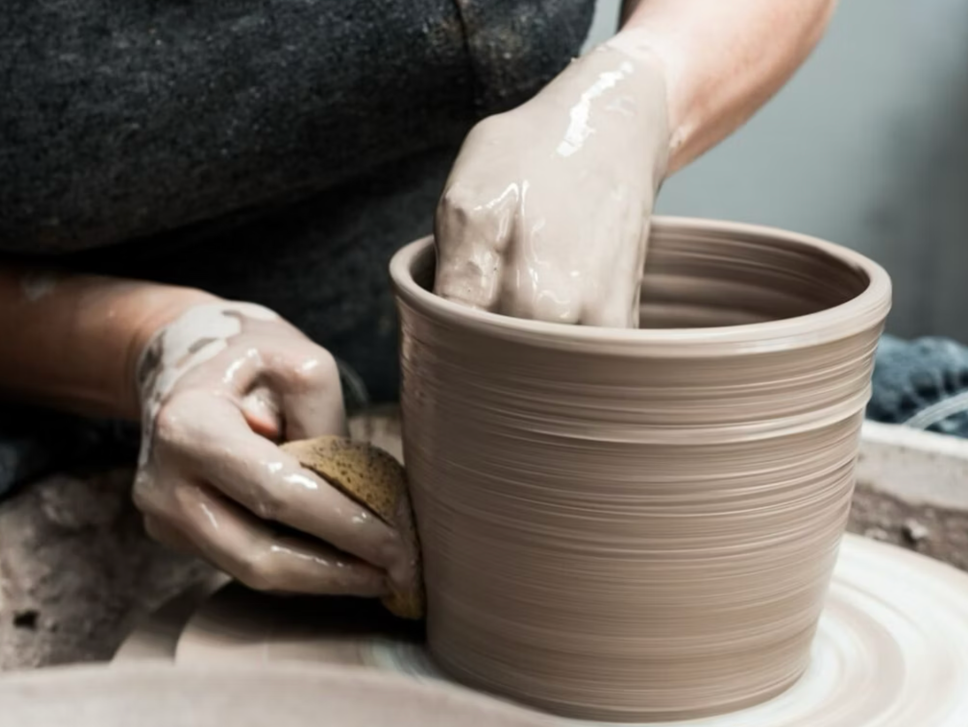 Close-up of hands shaping clay on a pottery wheel during a We Teach Me ceramics workshop.