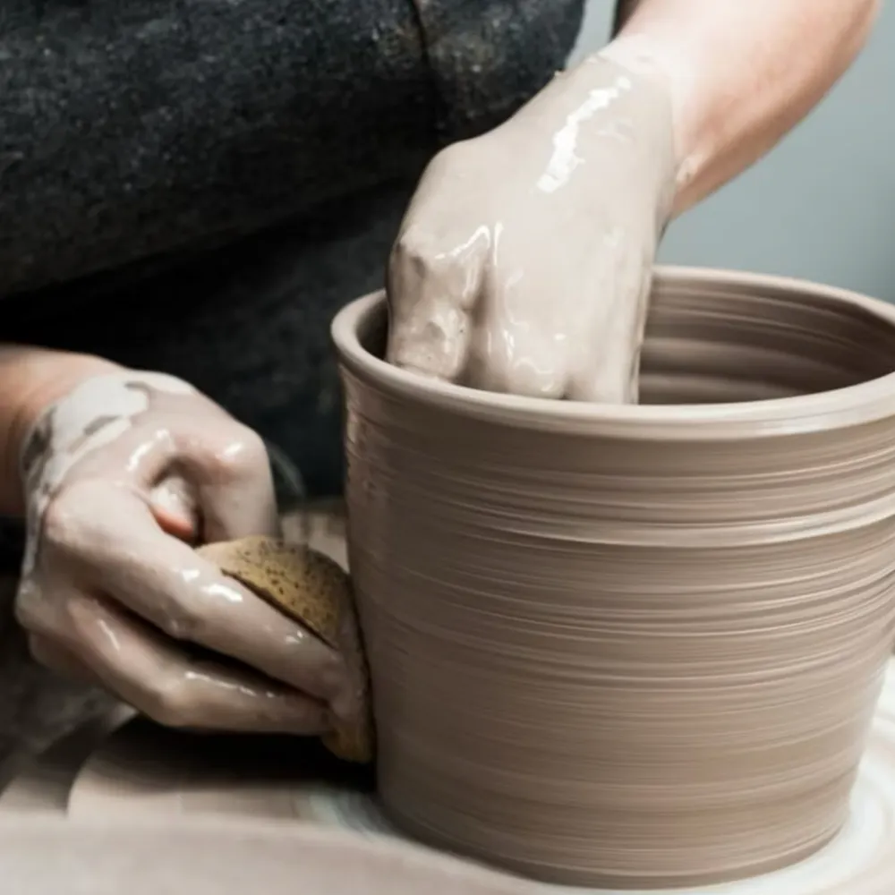 Close-up of hands shaping clay on a pottery wheel during a We Teach Me ceramics workshop.