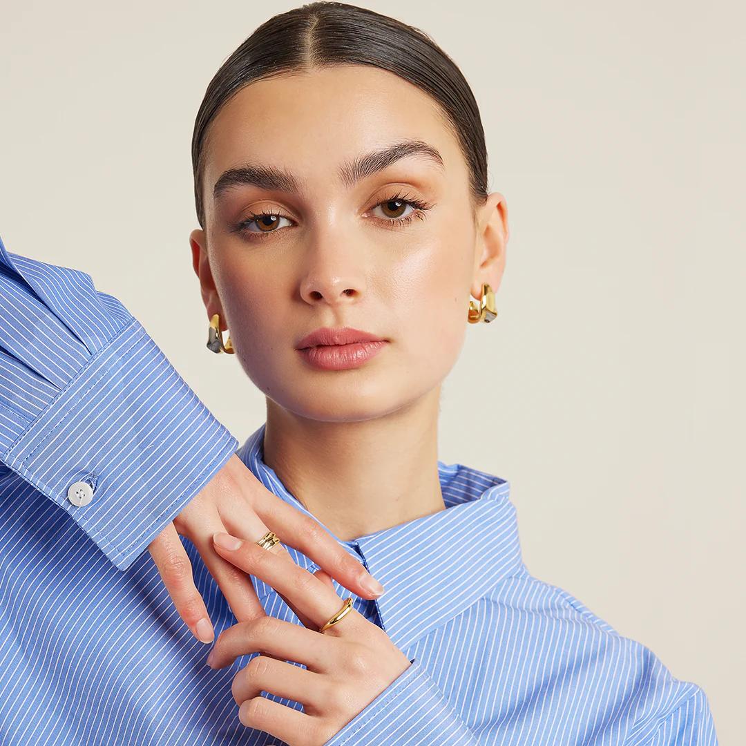 Francesca jewellery campaign, model wearing gold hoop earrings and rings styled with a blue striped shirt
