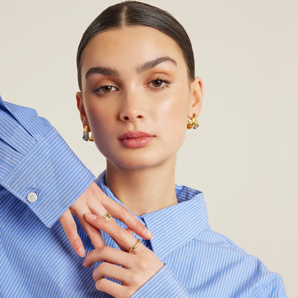 Francesca jewellery campaign, model wearing gold hoop earrings and rings styled with a blue striped shirt