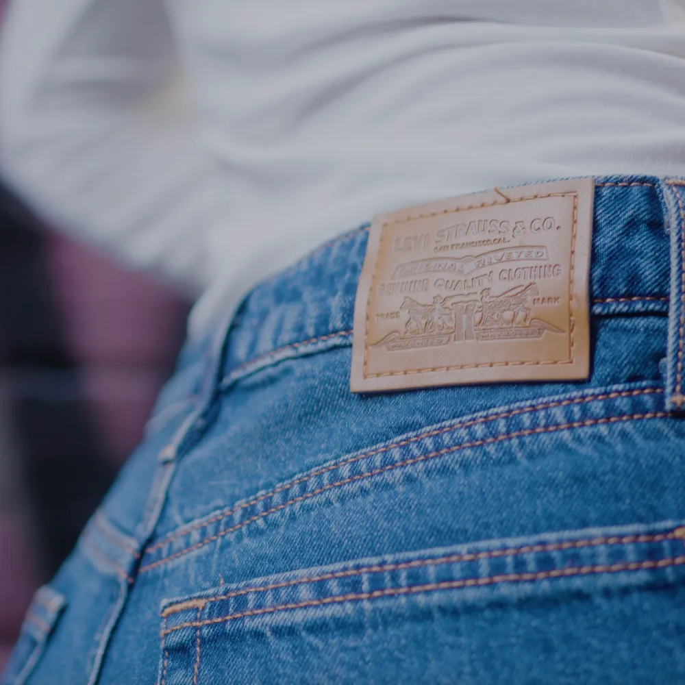 Back view of Levi’s Strauss & Co. classic blue denim jeans with brown leather patch branding, styled with a white top.