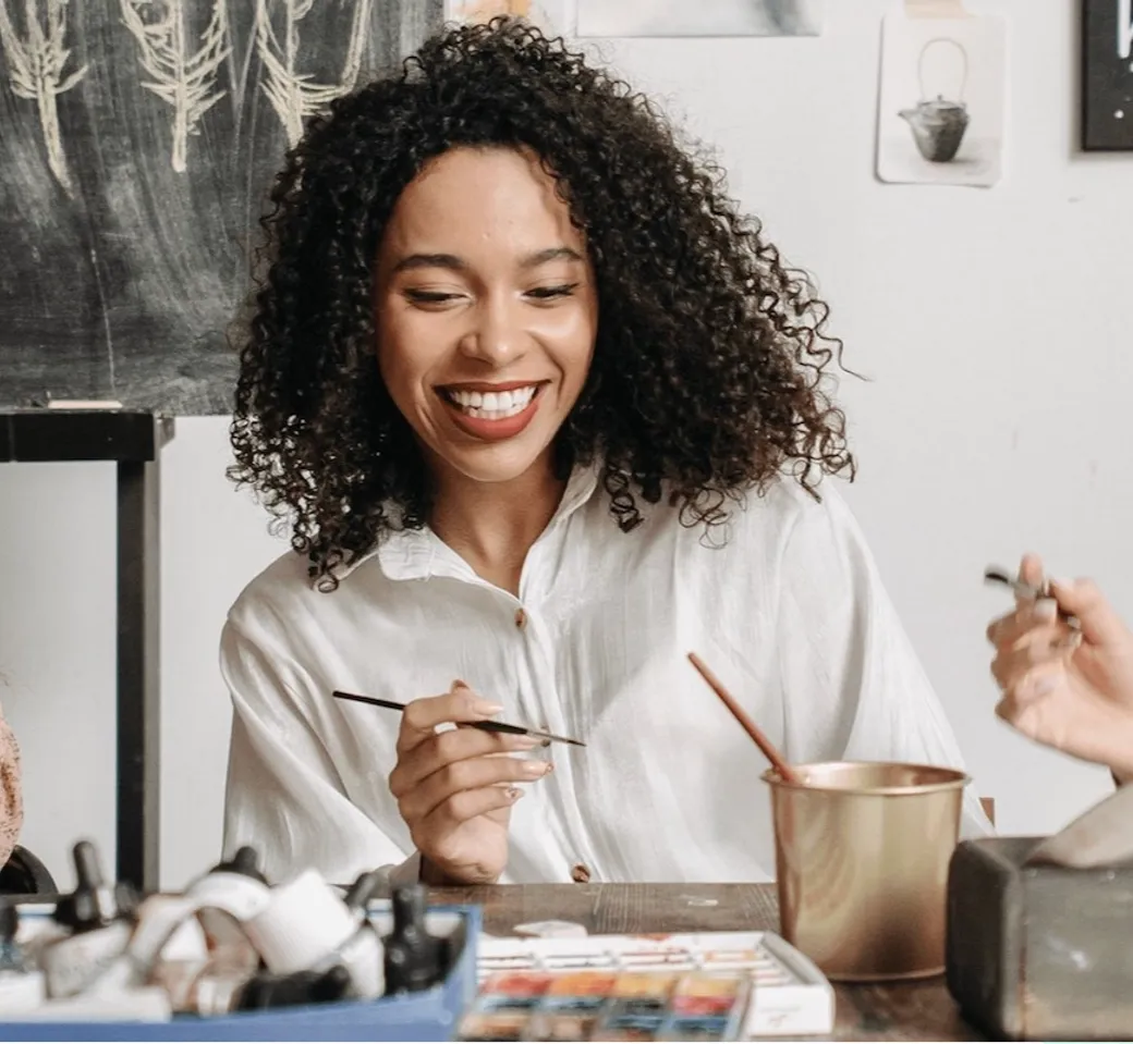 Smiling woman painting during a WeTeachMe creative class, holding a brush at a studio table.