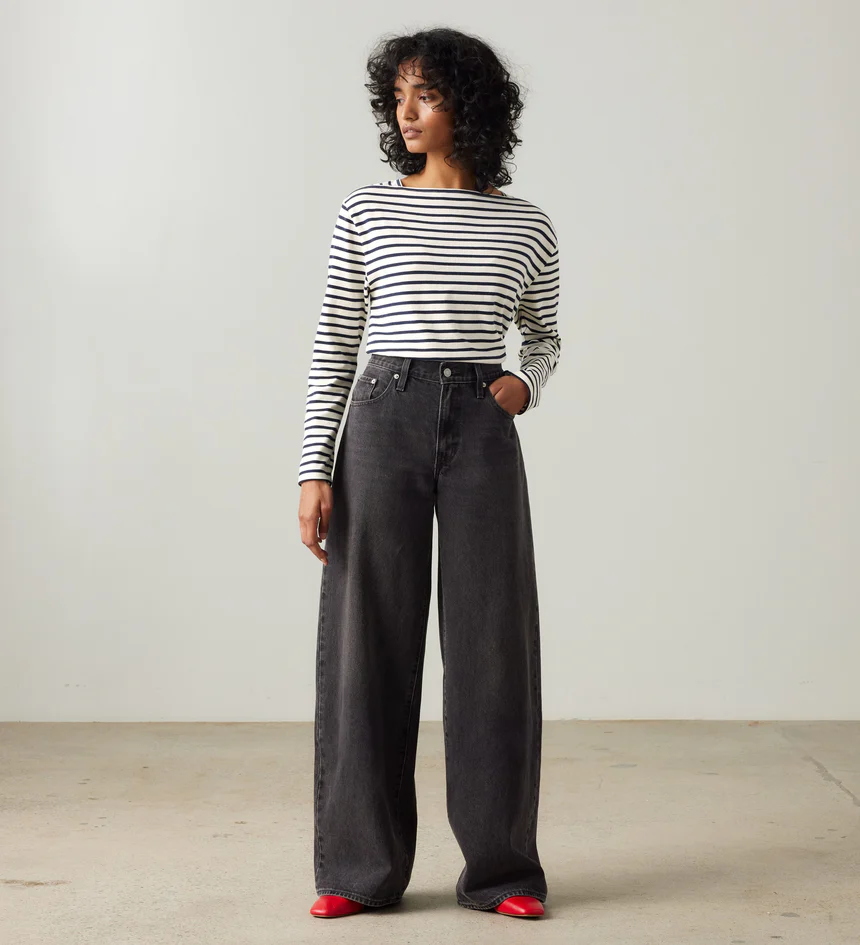 Model wearing Levi’s wide-leg black jeans styled with striped long sleeve top and red shoes against minimal studio background