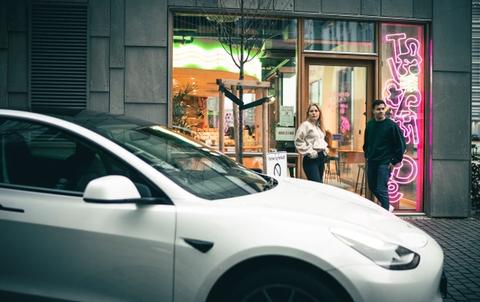 Tesla model 3 utenfor butikk, med trendy par i bakgrunn