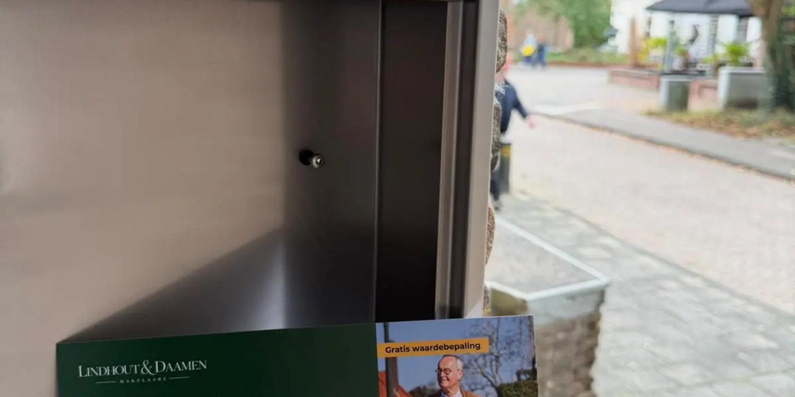 Persoonlijke kaart met QR-code steekt uit een metalen brievenbus aan een bakstenen gevel in een Nederlandse straat